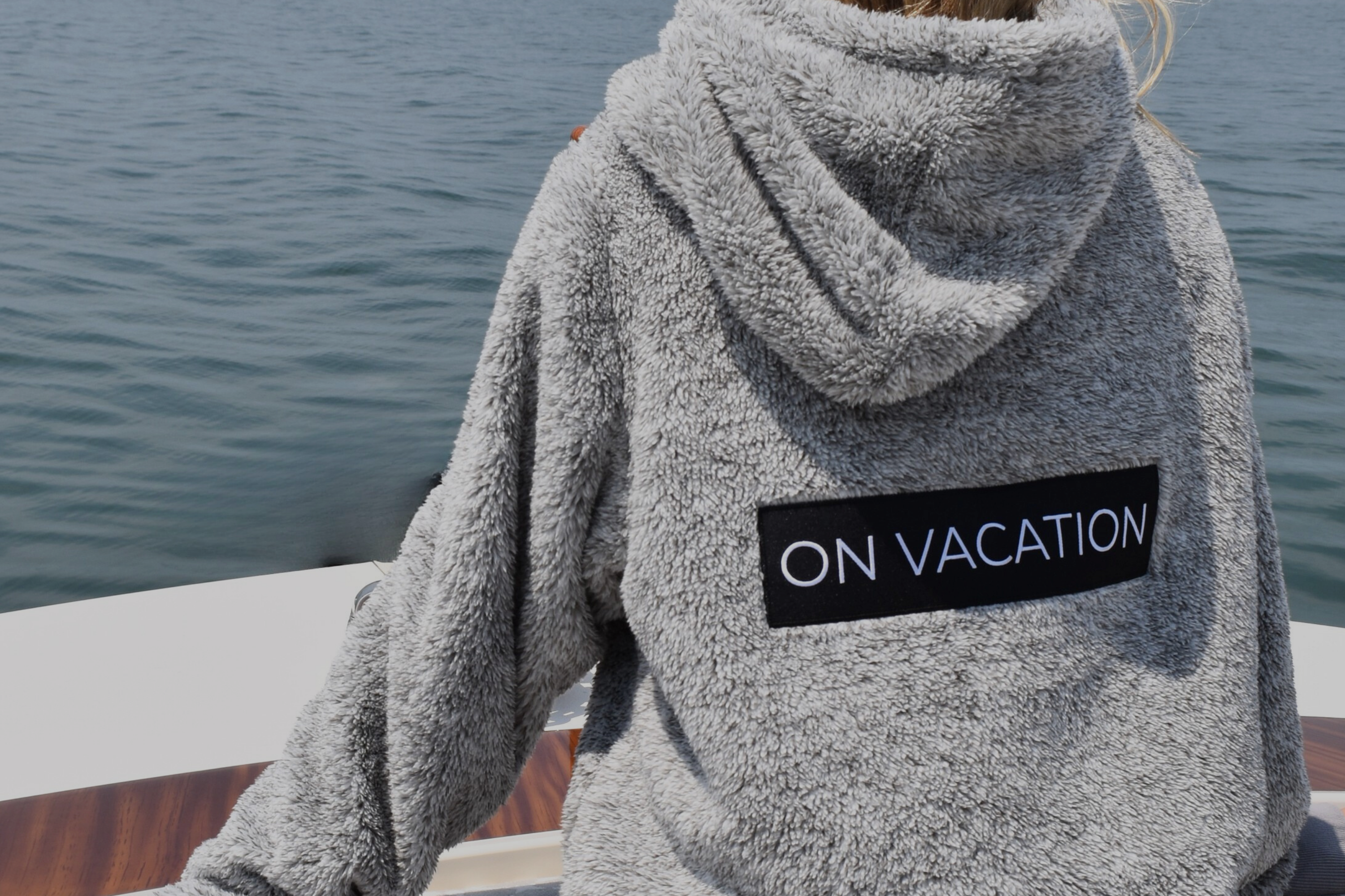 girl on boat wearing a grey sherpa hoodie that says "on vacation" in block letters on the back