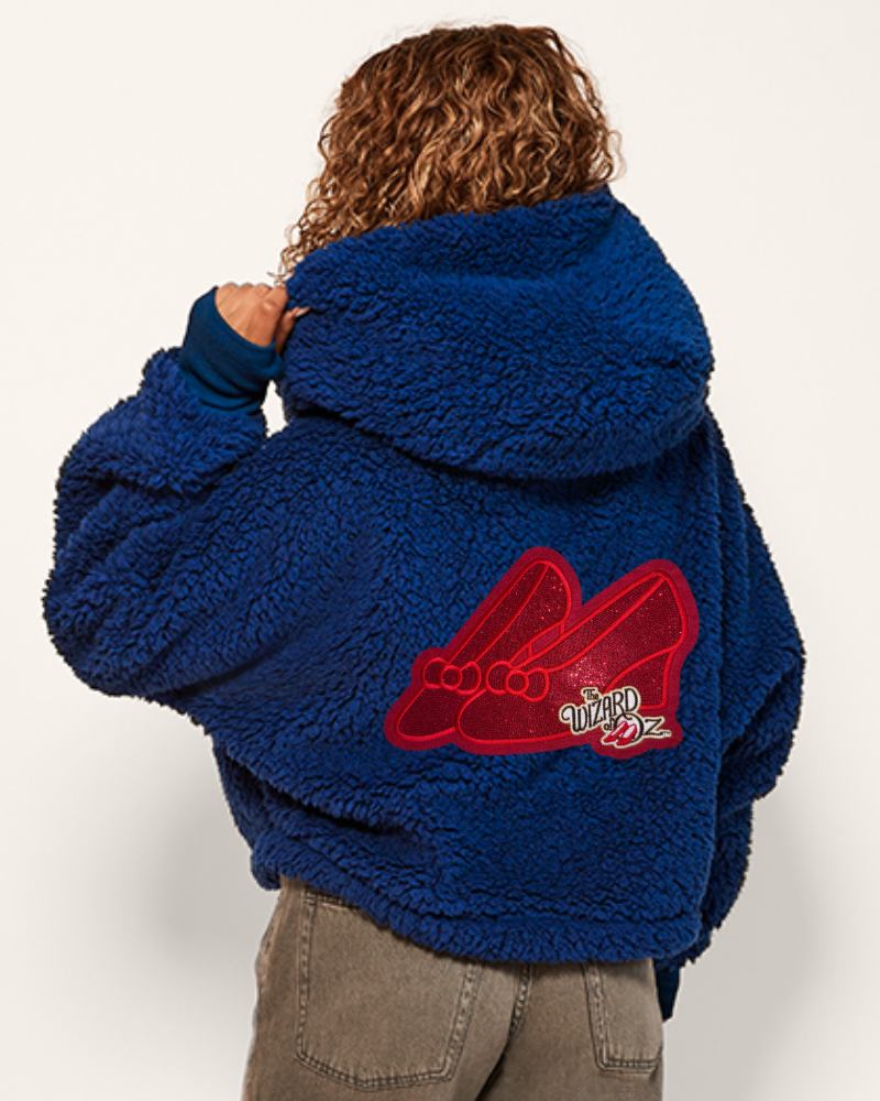 Person wearing a blue fleece jacket with a red 'Wizard of Oz' logo on the back.