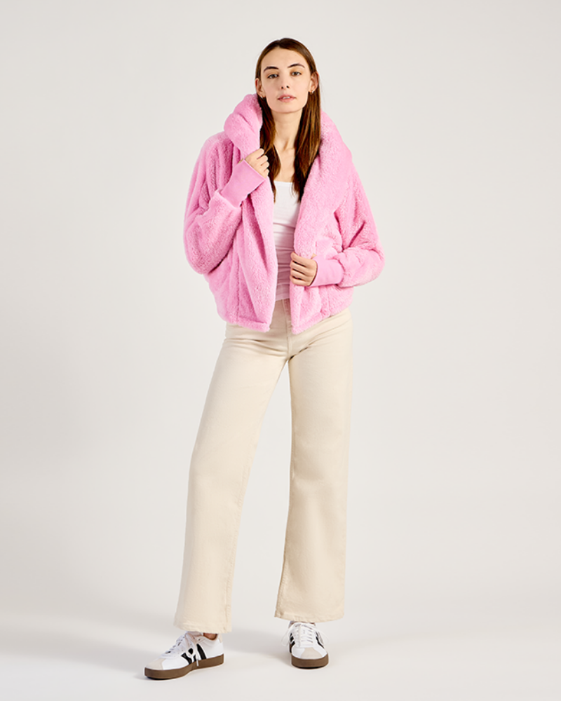 Woman wearing a pink jacket, white top, and beige pants on a white background