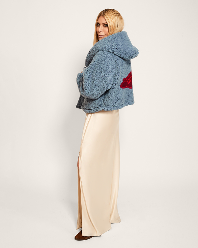 Woman wearing a blue fluffy jacket with a red heart design on a plain background