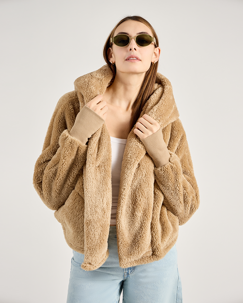 Woman wearing a beige teddy coat and sunglasses on a plain background
