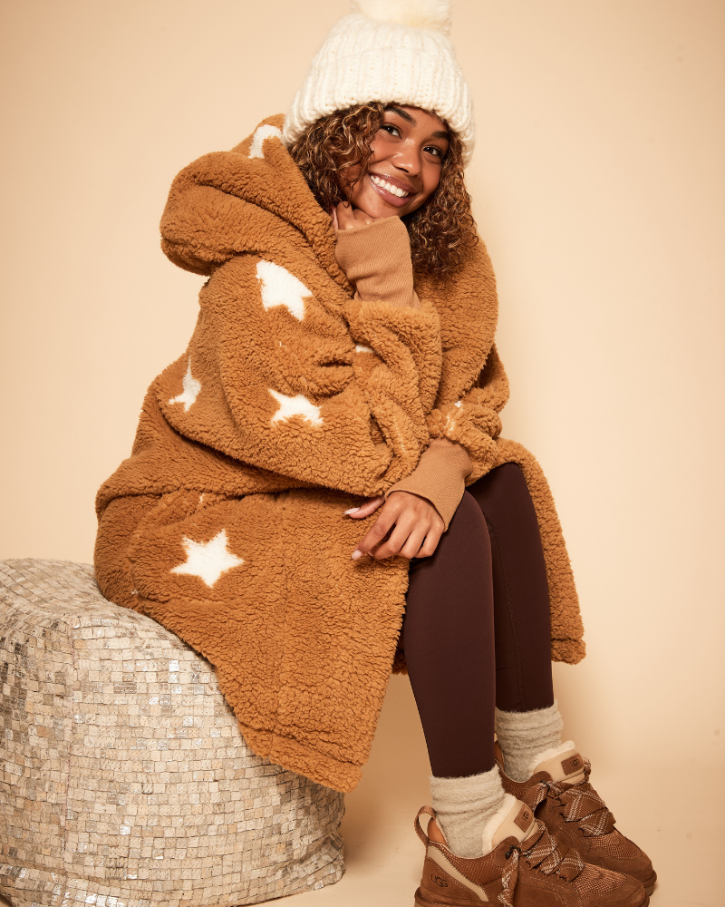 Person wearing a brown fleece blanket with star patterns, sitting on a textured surface.