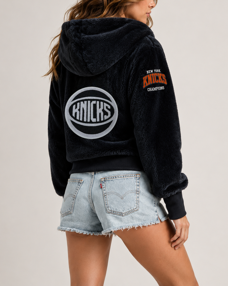 Person wearing a black hoodie with 'Knicks' branding on a plain background