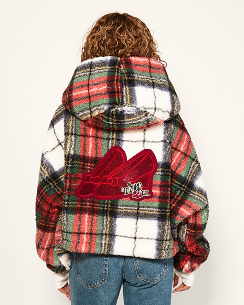 Person wearing a plaid jacket with a red logo on the back, standing against a white background