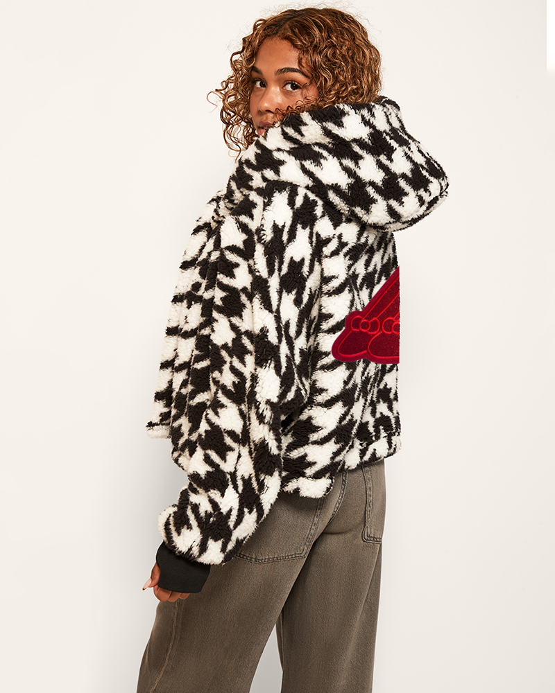 Person wearing a black and white patterned jacket with a red heart design on a plain background