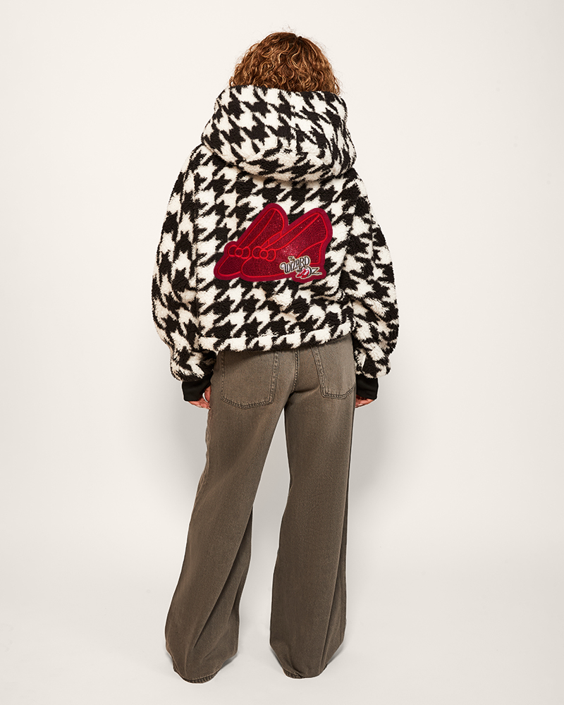 Person wearing a houndstooth pattern jacket with a red logo on the back, standing against a white background.
