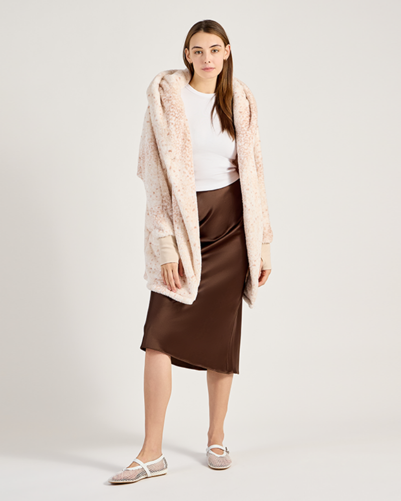 Woman wearing an ivory printed, white top, and brown skirt on a light gray background