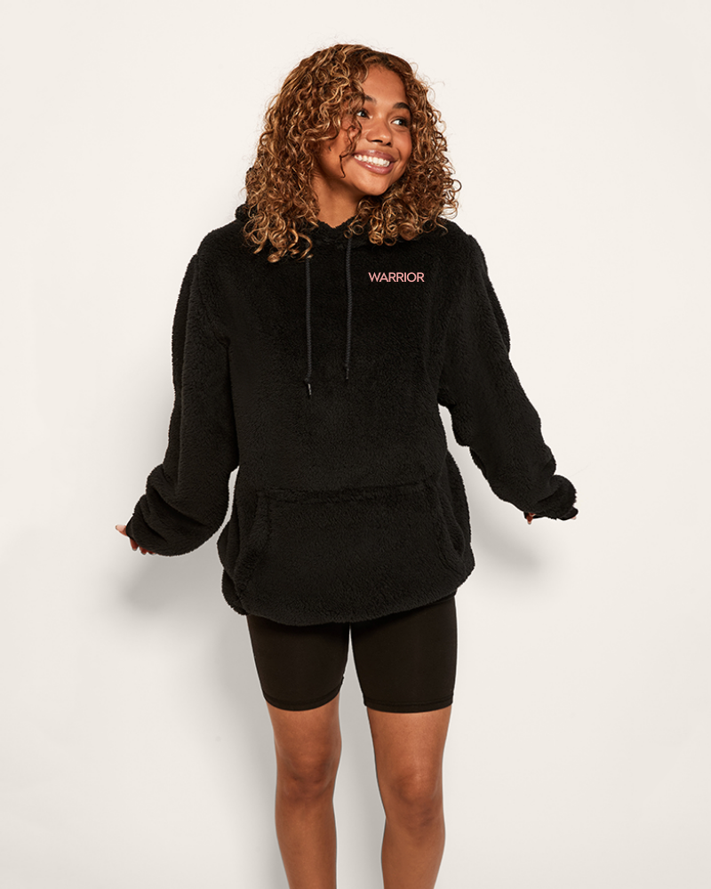 Woman wearing a black hoodie with 'Warrior' logo on a white background
