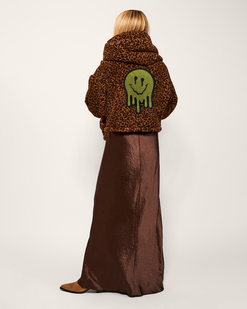 Person wearing a leopard print coat with a green smiley face design on a white background