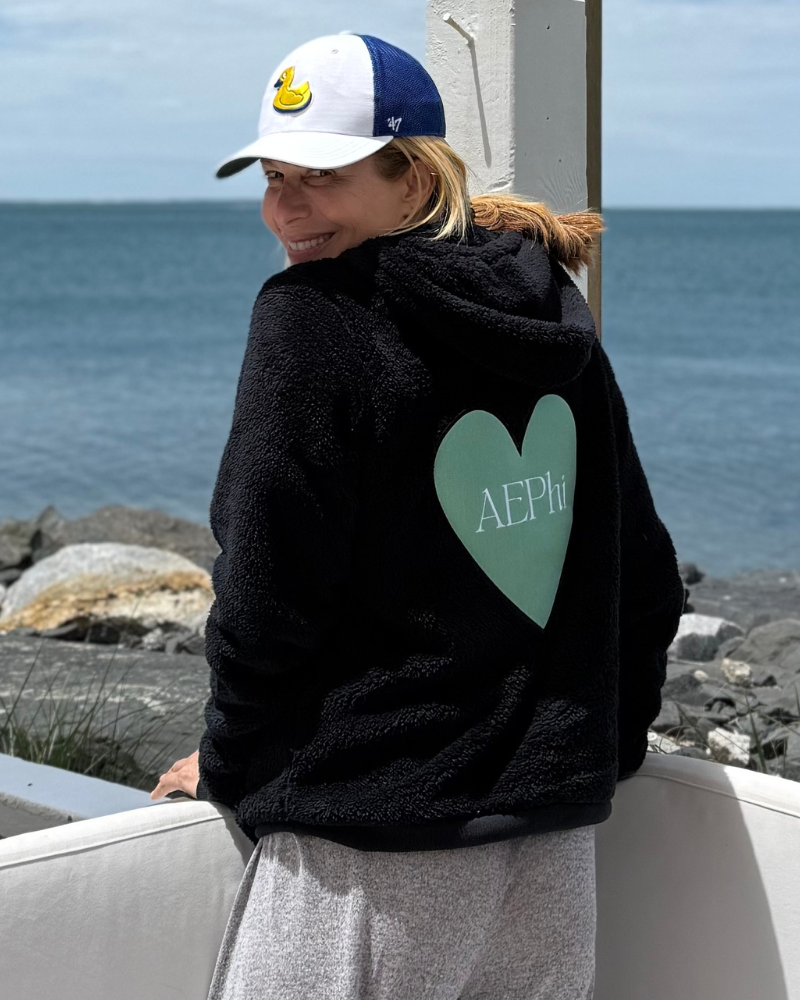 woman wearing black sherpa hoodie with oversized mint green heart patch that says "AEPhi"