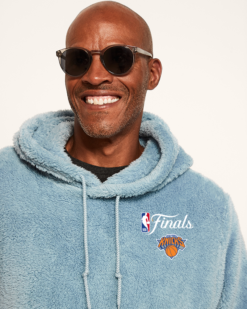 Man wearing a blue hoodie with NBA Finals logo and New York Knicks logo on a white background