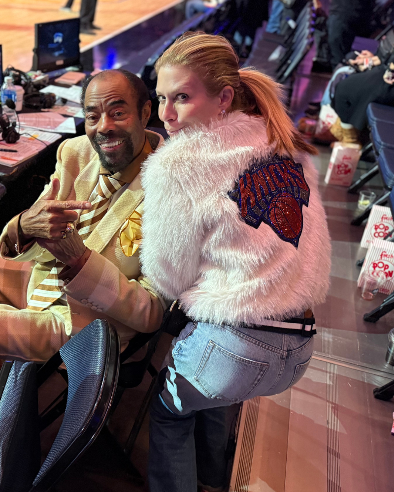 Two people sitting together in a casual setting, one wearing a fluffy jacket with a logo.