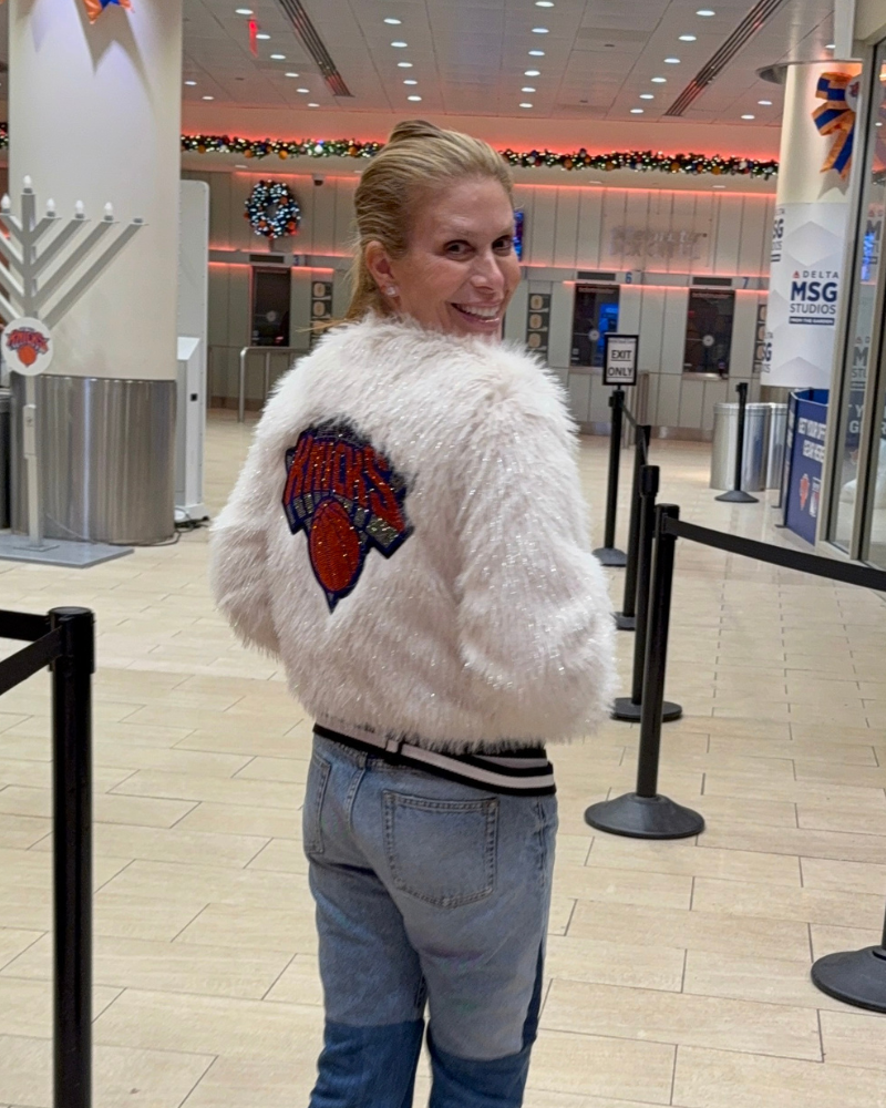 Person wearing a white fluffy jacket with a logo in an indoor setting