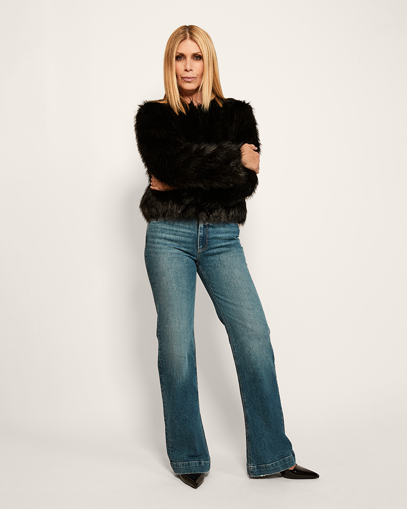 Woman wearing a black fur-trimmed sweater and blue jeans on a white background