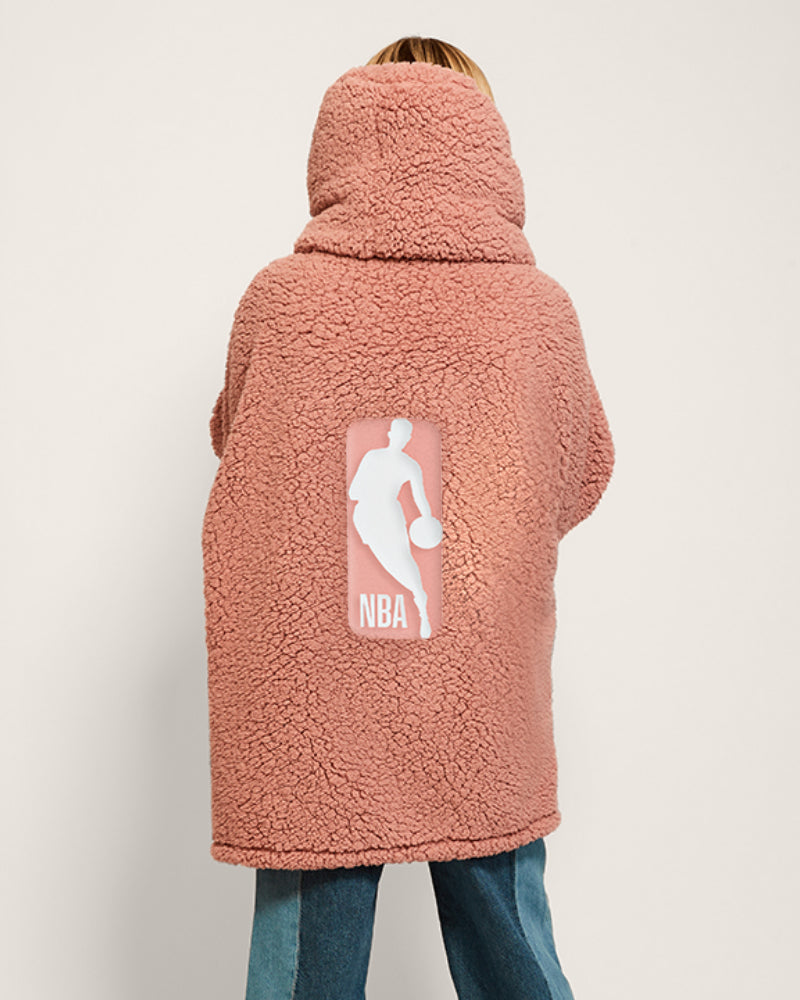 Person wearing a pink sherpa jacket with NBA logo on the back against a white background
