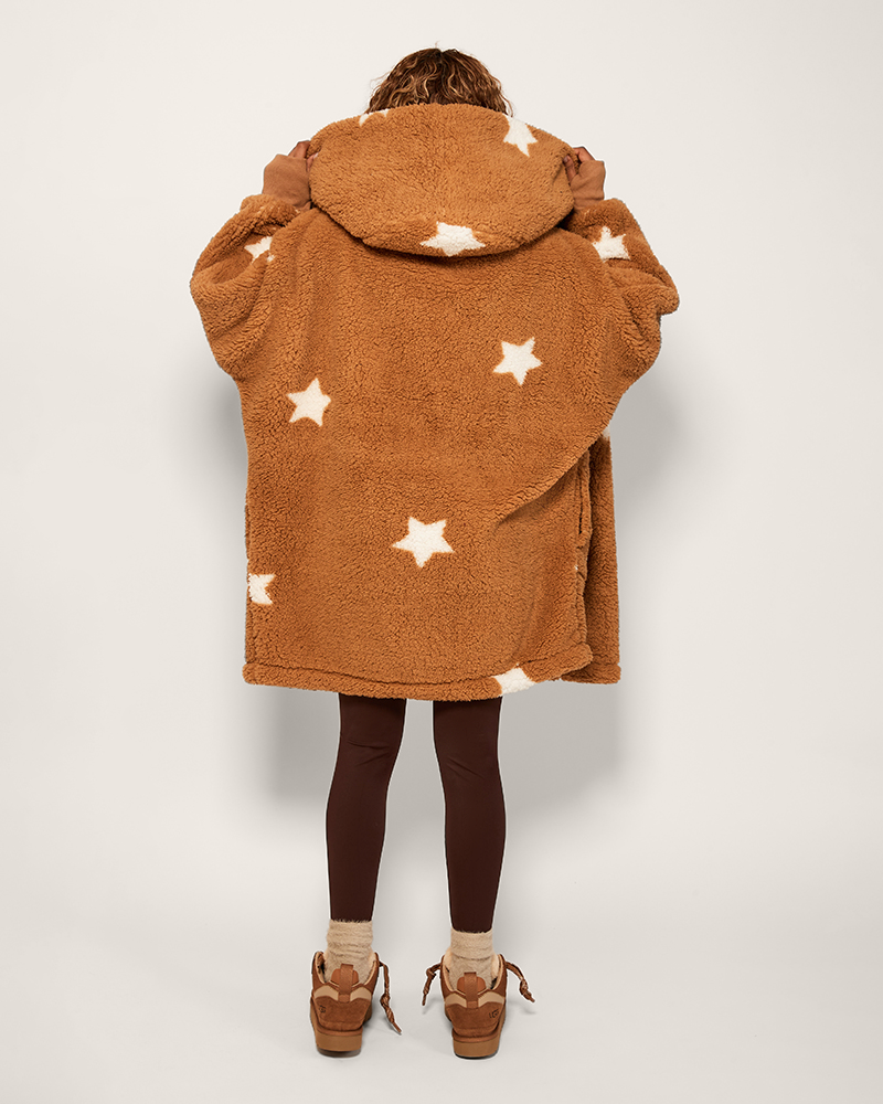 Brown fleece poncho with star patterns worn by a person on a plain background