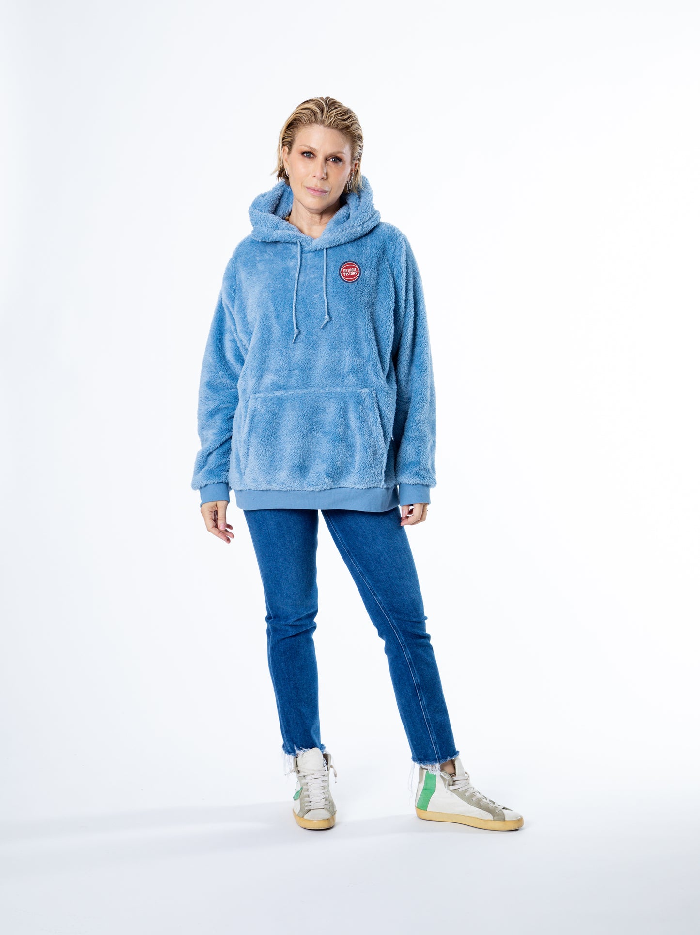 Woman facing forward wearing light blue sherpa hoodie with a front kangaroo pocket and drawstring hood, featuring small circular Detroit Pistons embroidery on the left chest.