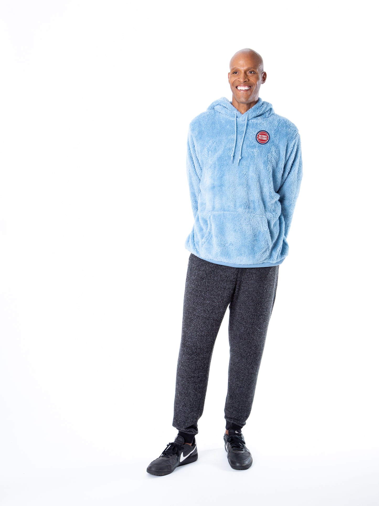 Man facing forward wearing light blue sherpa hoodie with a front kangaroo pocket and drawstring hood, featuring small circular Detroit Pistons embroidery on the left chest.