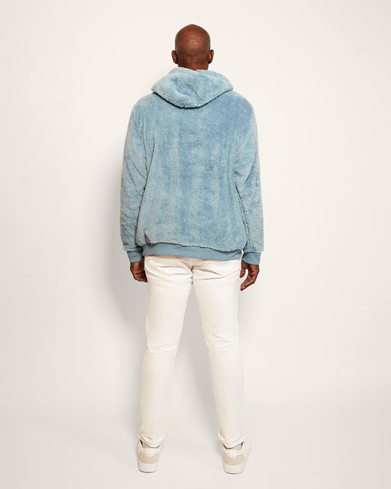Person wearing a blue hoodie and white pants on a light gray background