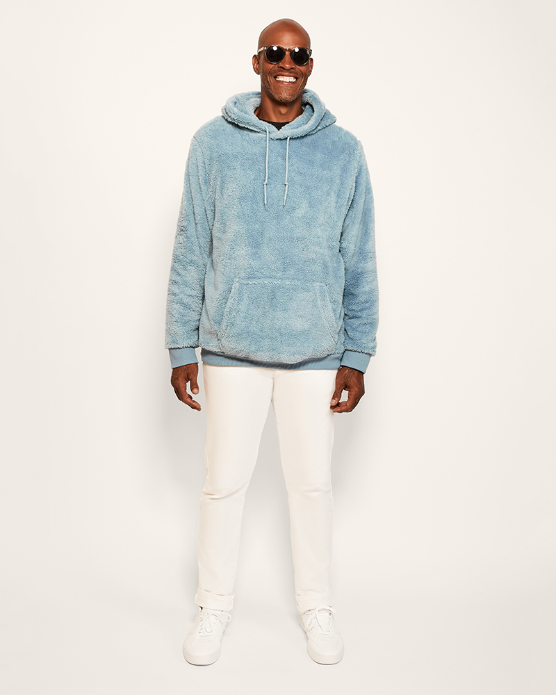 Man wearing a blue hoodie and white pants on a white background