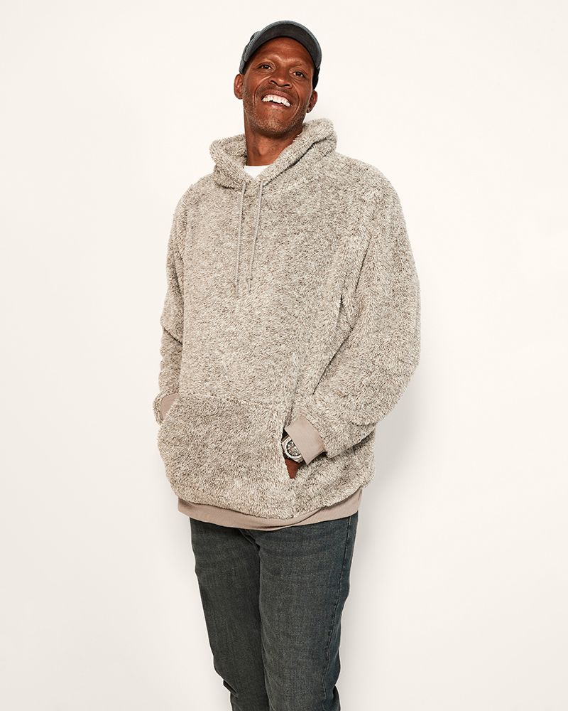 Man wearing a grey hoodie and dark pants on a white background