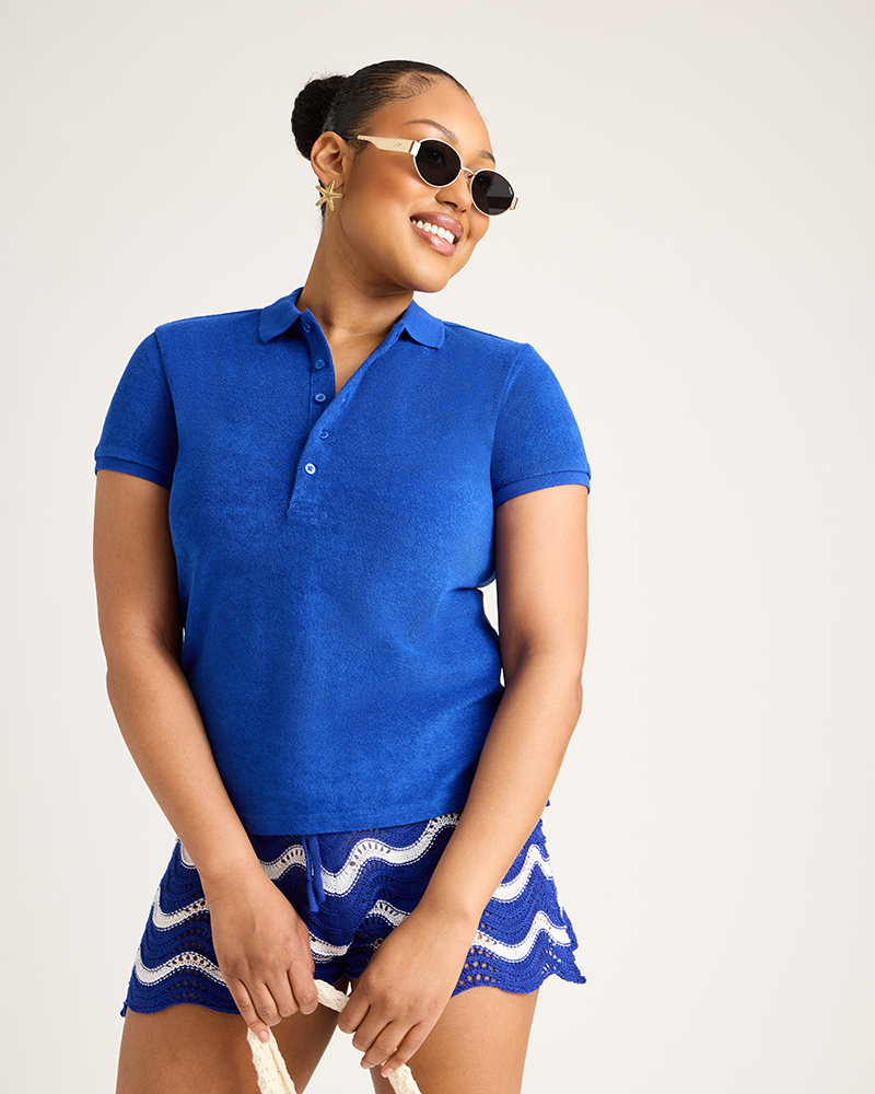 Woman wearing a blue polo shirt and patterned shorts with sunglasses on a plain background|Model: 5'9 wearing size L