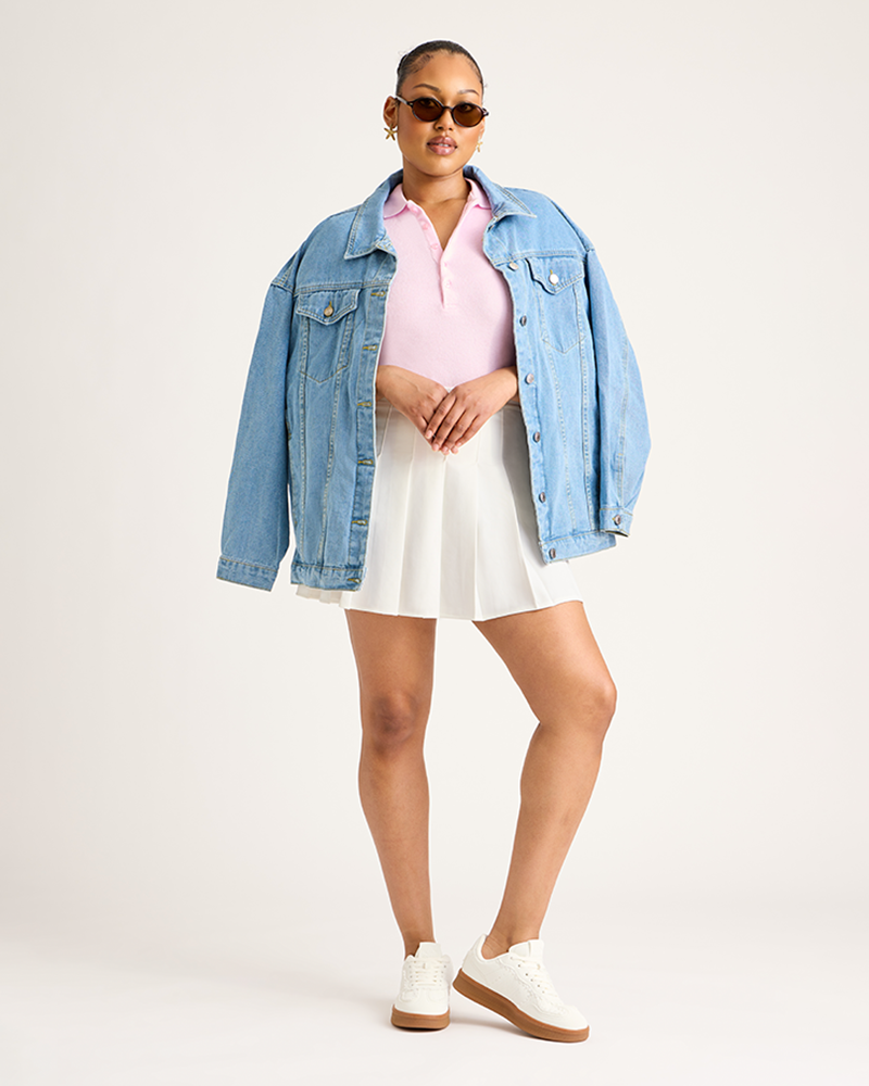 Woman wearing a denim jacket, pink shirt, white skirt, and white sneakers on a plain background|Model: 5'9 wearing size L