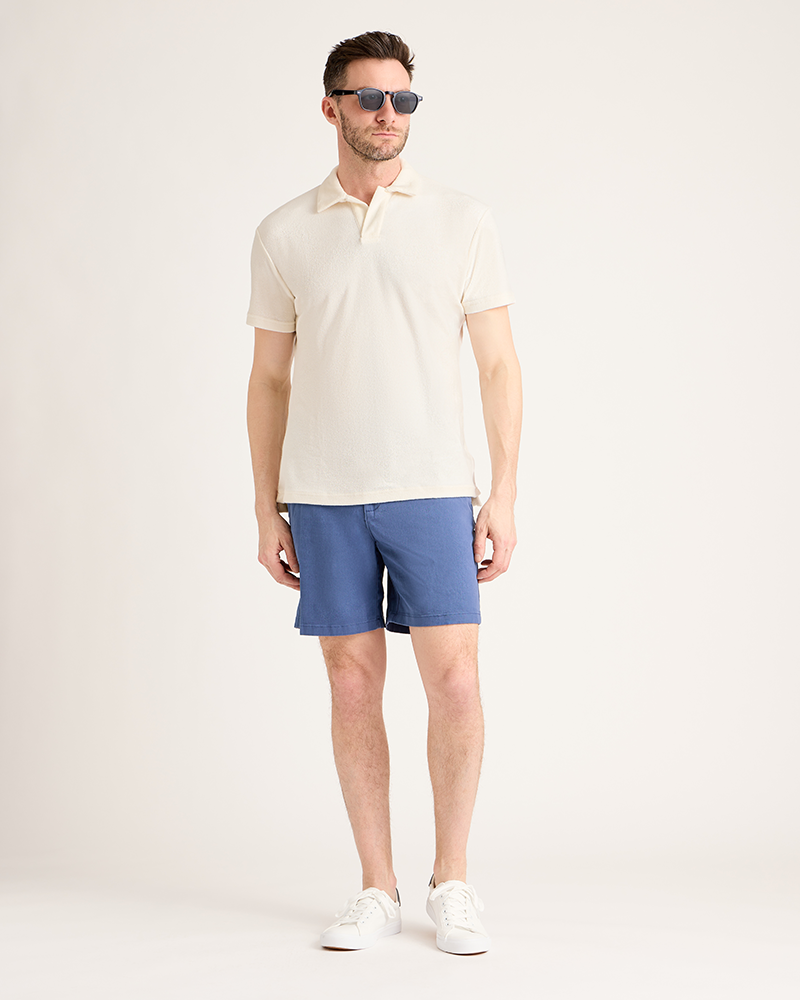 Man wearing a cream polo shirt and blue shorts on a white background|Model: 5'11" wearing size L