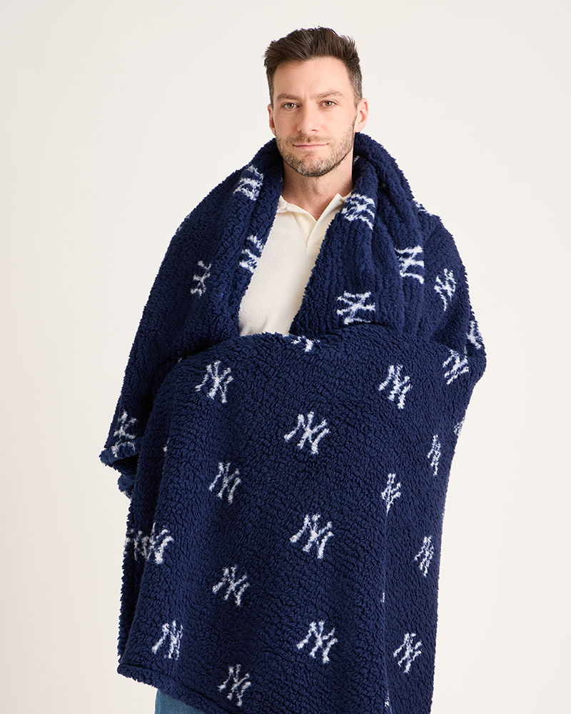 Man wrapped in a navy blue blanket with white logos on a light gray background