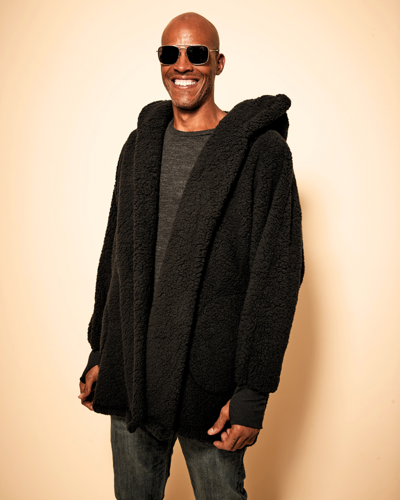 Man wearing a black hooded lounger and sunglasses against a beige background