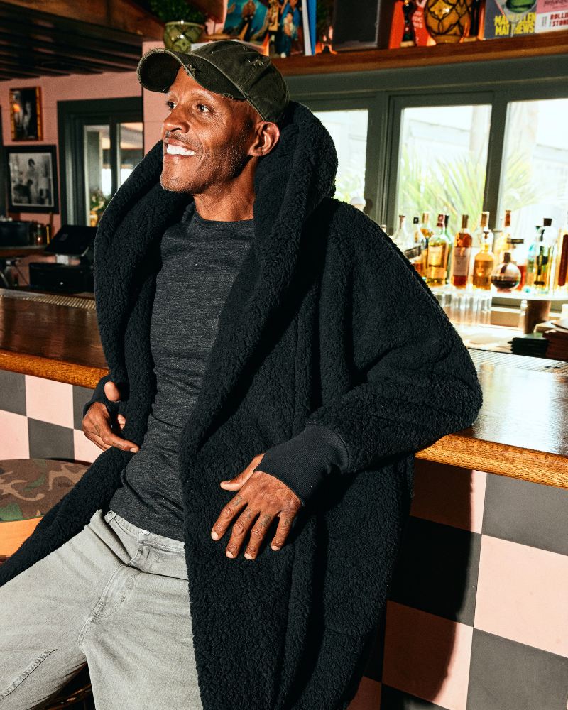 man wearing black sherpa hooded lounger sitting on bar stool against bar in restaurant