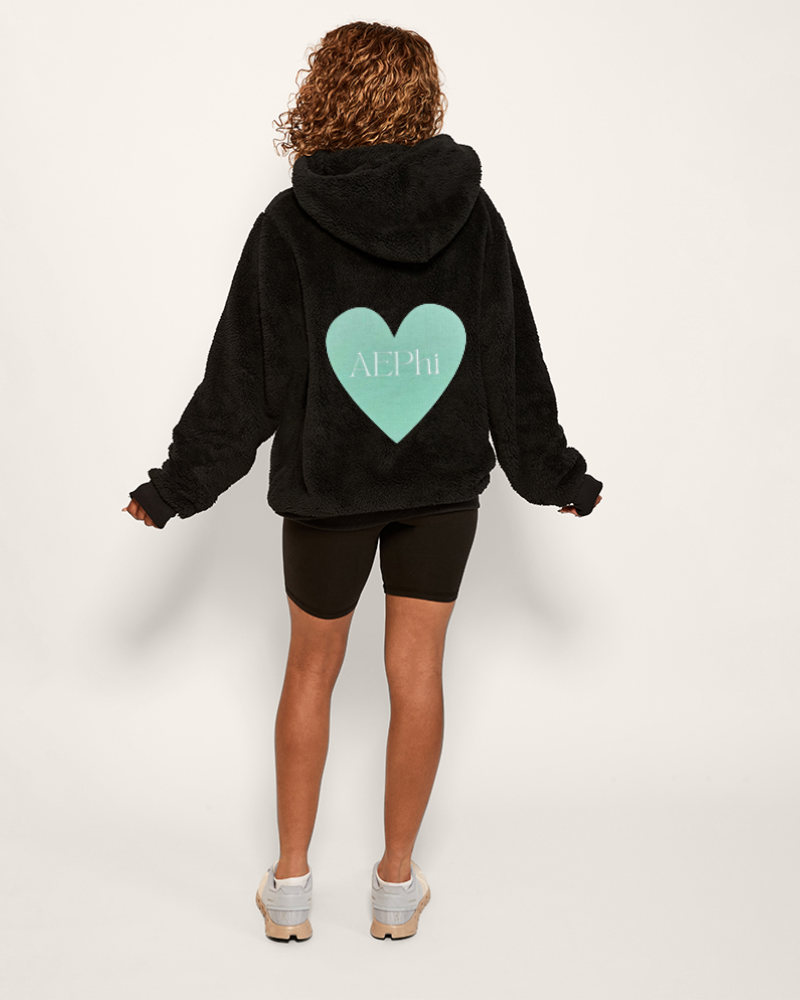 woman wearing black sherpa hoodie with oversized mint green heart patch that says "AEPhi"