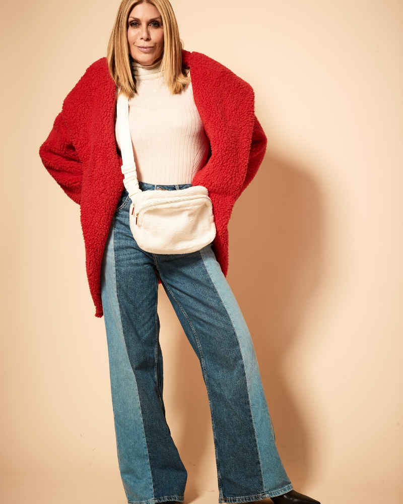 Person wearing a red cardigan, white top, and blue jeans with a beige bag on a beige background