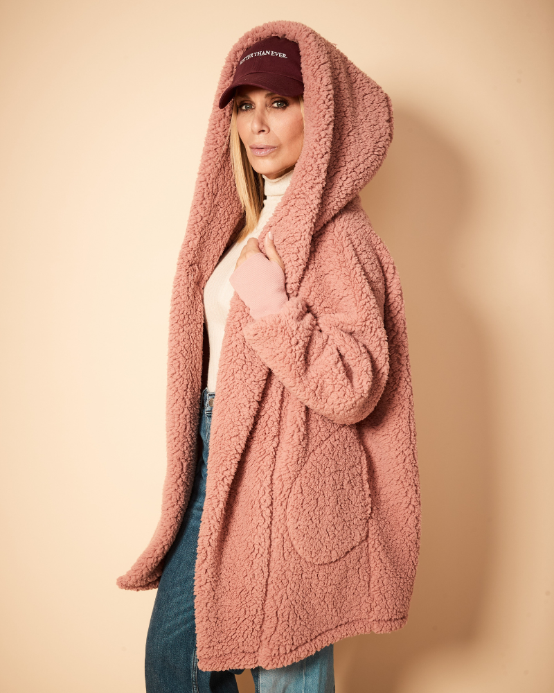 Person wearing a pink hooded coat against a beige background