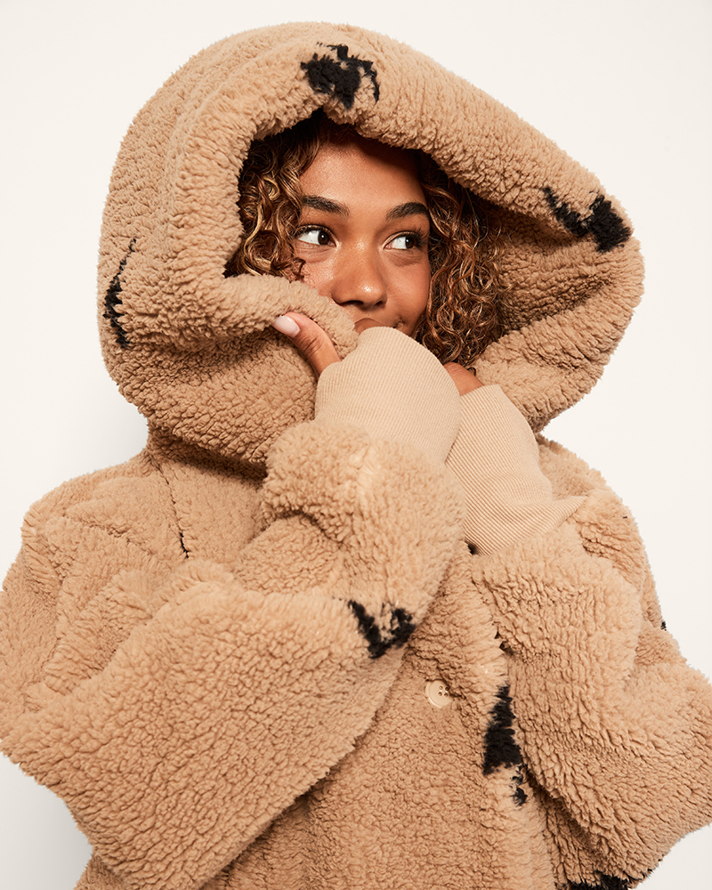 Person wearing a beige sherpa coat with black accents on a white background