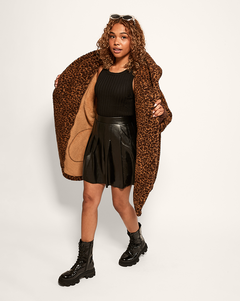 person wearing leopard sherpa lounger over black top and skirt against light background
