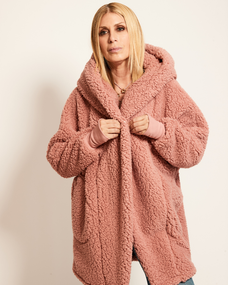 Woman wearing a pink teddy coat against a plain background