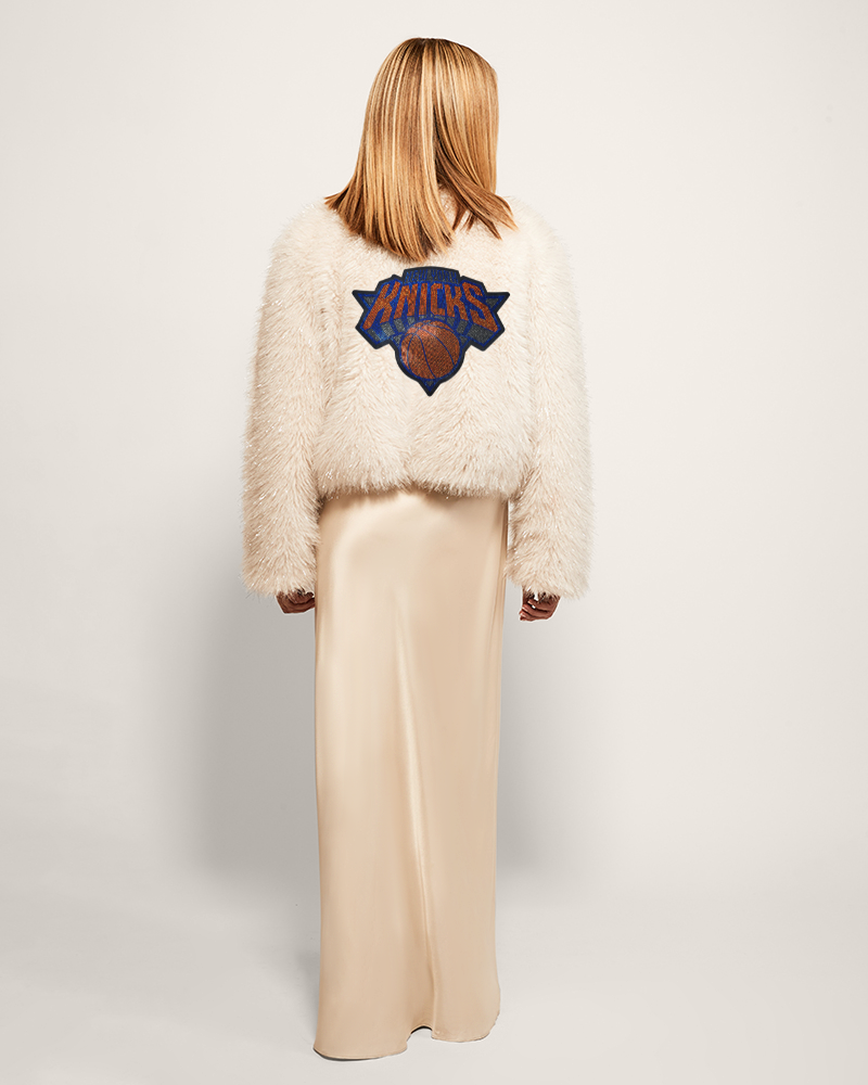 Person wearing a fluffy white jacket with a logo on the back against a plain background