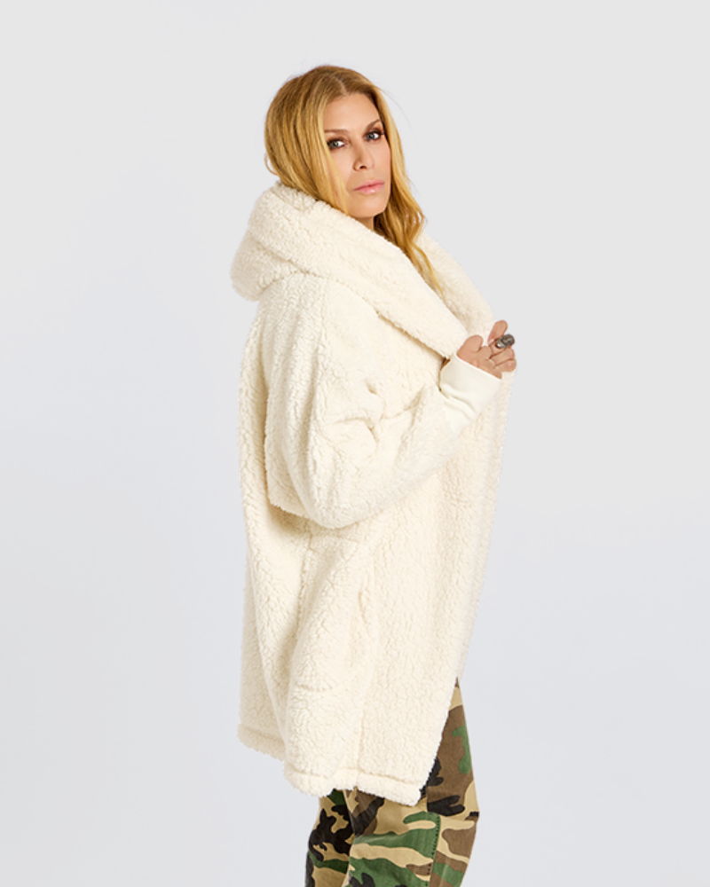 A woman modeling a cream sherpa fleece hooded jacket with a large plush collar, paired with camouflage pants, against a light gray studio background.|Jill is 5'6" wearing size XS/S