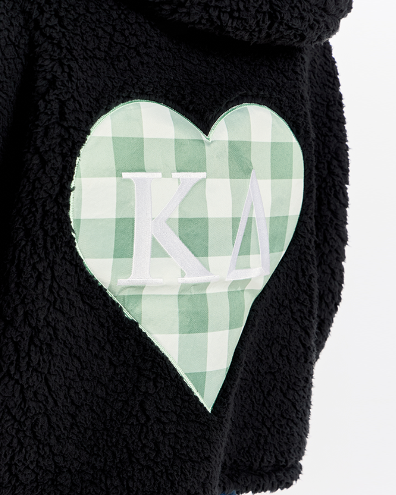 Close-up of a black sherpa fleece garment featuring a large heart-shaped patch with a green and white gingham pattern and white Greek letters 'Kappa Delta' in the center.
