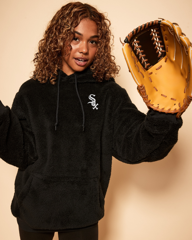 Person wearing a black hoodie with a chicago white sox logo, holding a baseball glove against a beige background