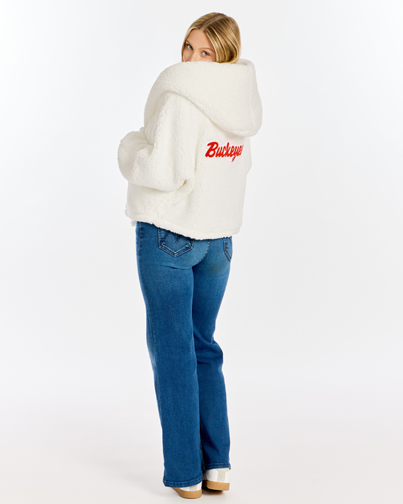 A woman wearing a white sherpa fleece cropped hoodie with a red 'Buckeyes' logo on the back, paired with blue jeans, photographed from behind against a white studio background.