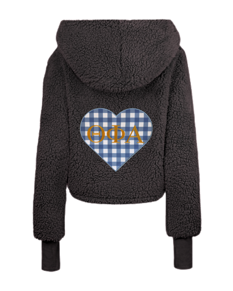 A black sherpa fleece cropped hoodie shown from the back, featuring a blue and white gingham heart graphic with the Greek letters 'Theta Phi Alpha' in gold in the center.