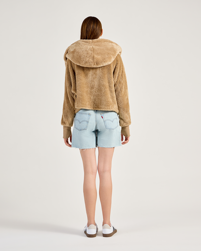 Person wearing a beige fleece jacket and light blue denim shorts on a white background