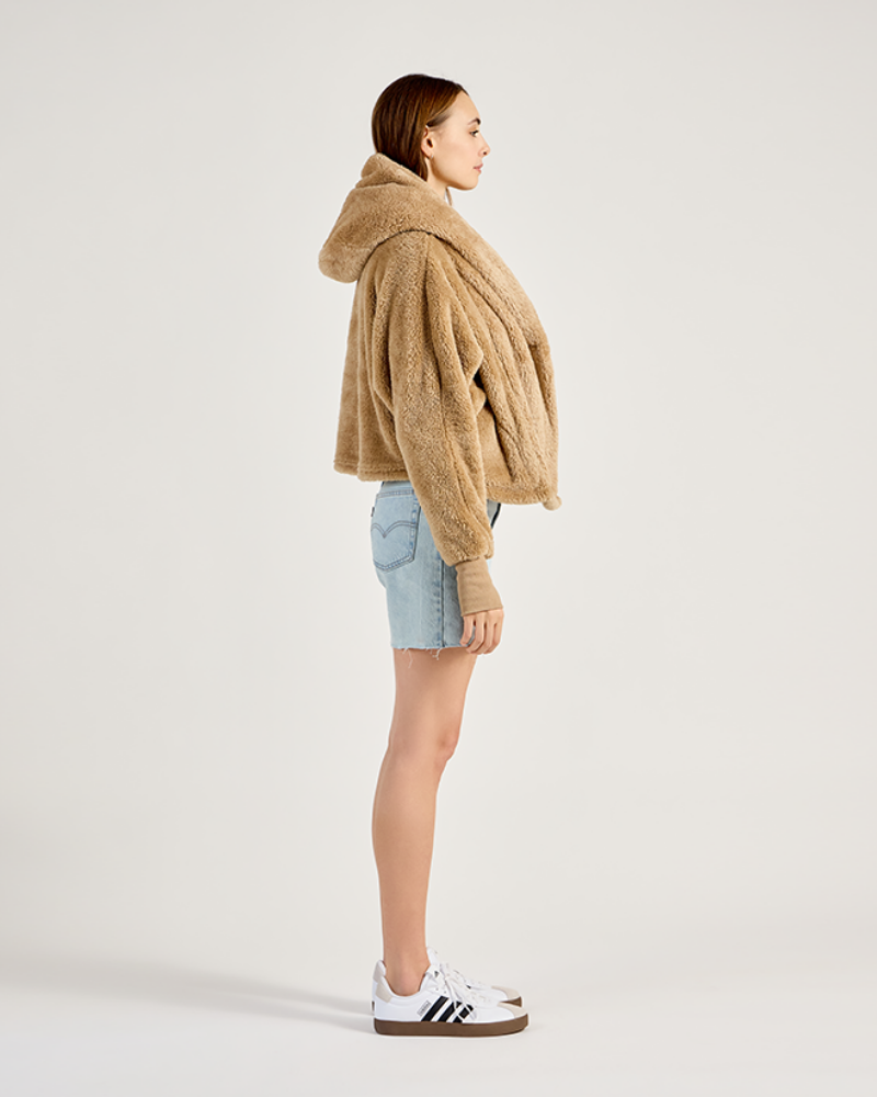 Person wearing a beige oversized hoodie with denim shorts on a white background