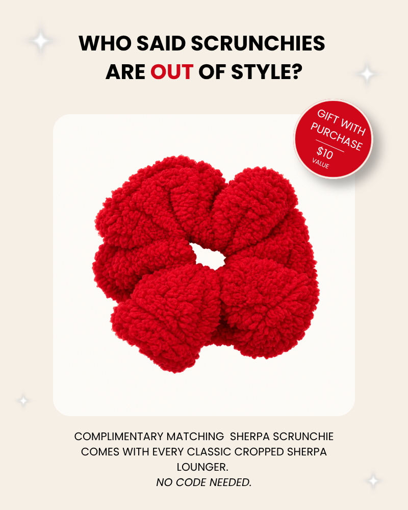 A red sherpa scrunchie centered on a cream background with promotional text above and below. The text reads 'WHO SAID SCRUNCHIES ARE OUT OF STYLE?' and 'COMPLIMENTARY MATCHING SHERPA SCRUNCHIE COMES WITH EVERY CLASSIC CROPPED SHERPA LOUNGER.