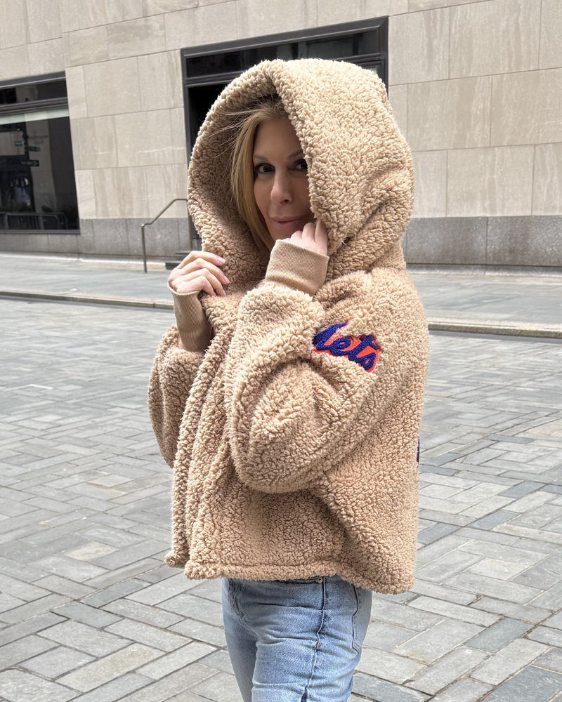 Person wearing a beige fleece hoodie with a brand logo outdoors on a stone pavement.|Jill: 5'6" in size XS/S