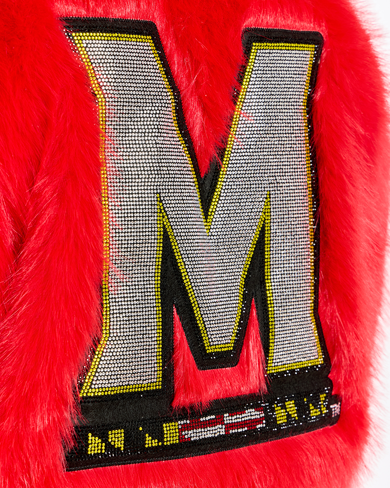 A close-up of a bright red fuzzy garment featuring a large bedazzled letter 'M' embellished with silver rhinestones, outlined in black and yellow.