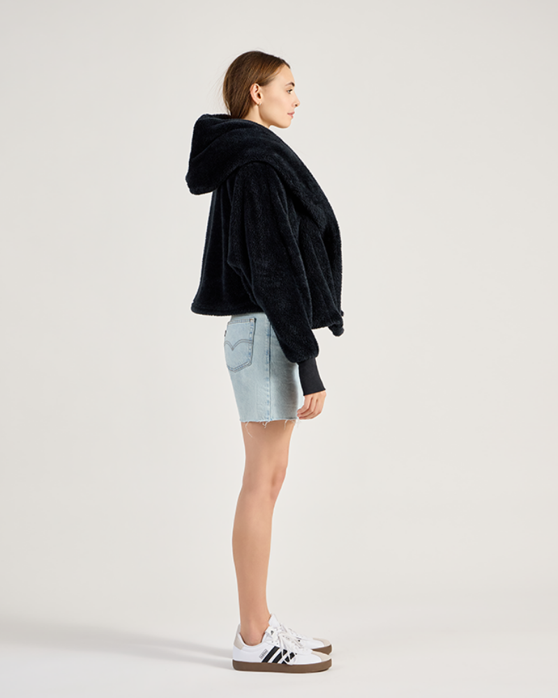 Person wearing a black hoodie and light blue shorts on a white background