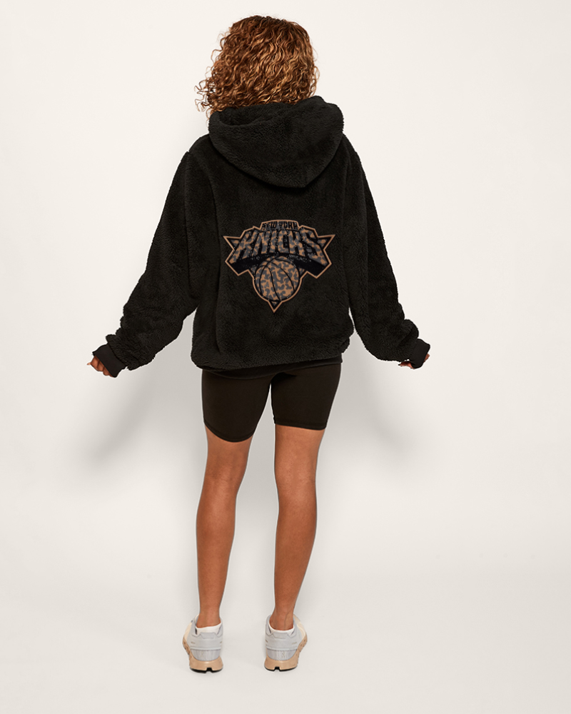 girl wearing black hoodie with bedazzled leopard printed new york knicks logo on back